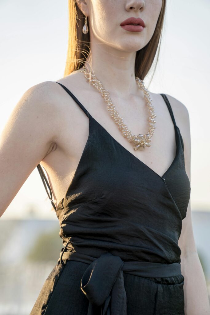 A stylish woman wearing elegant jewelry and a black dress in an outdoor setting.